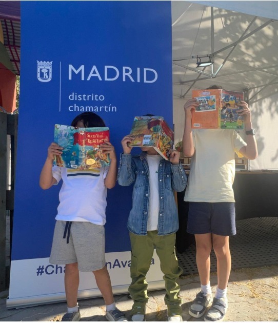 niños posando con un libro en la cara ante un cartel de la junta de Chamartín