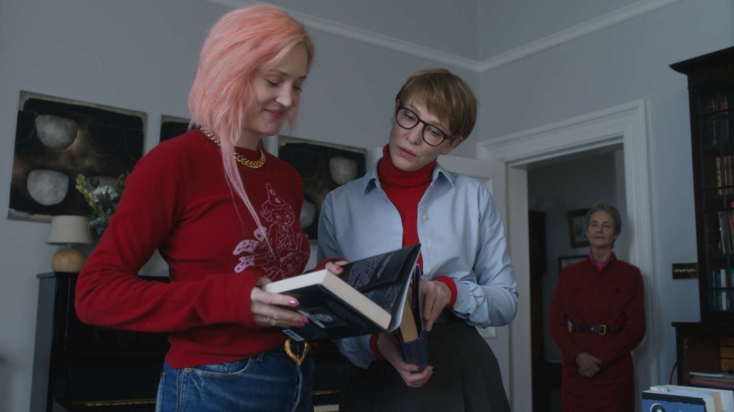 Escena de la película “Father Mother Sister Brother” de Jim Jarmusch con dos mujeres revisando un libro en un salón.