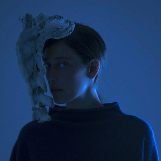 Retrato conceptual de una persona con iluminación azul y un elemento escultórico cubriendo parte del rostro de María Coma